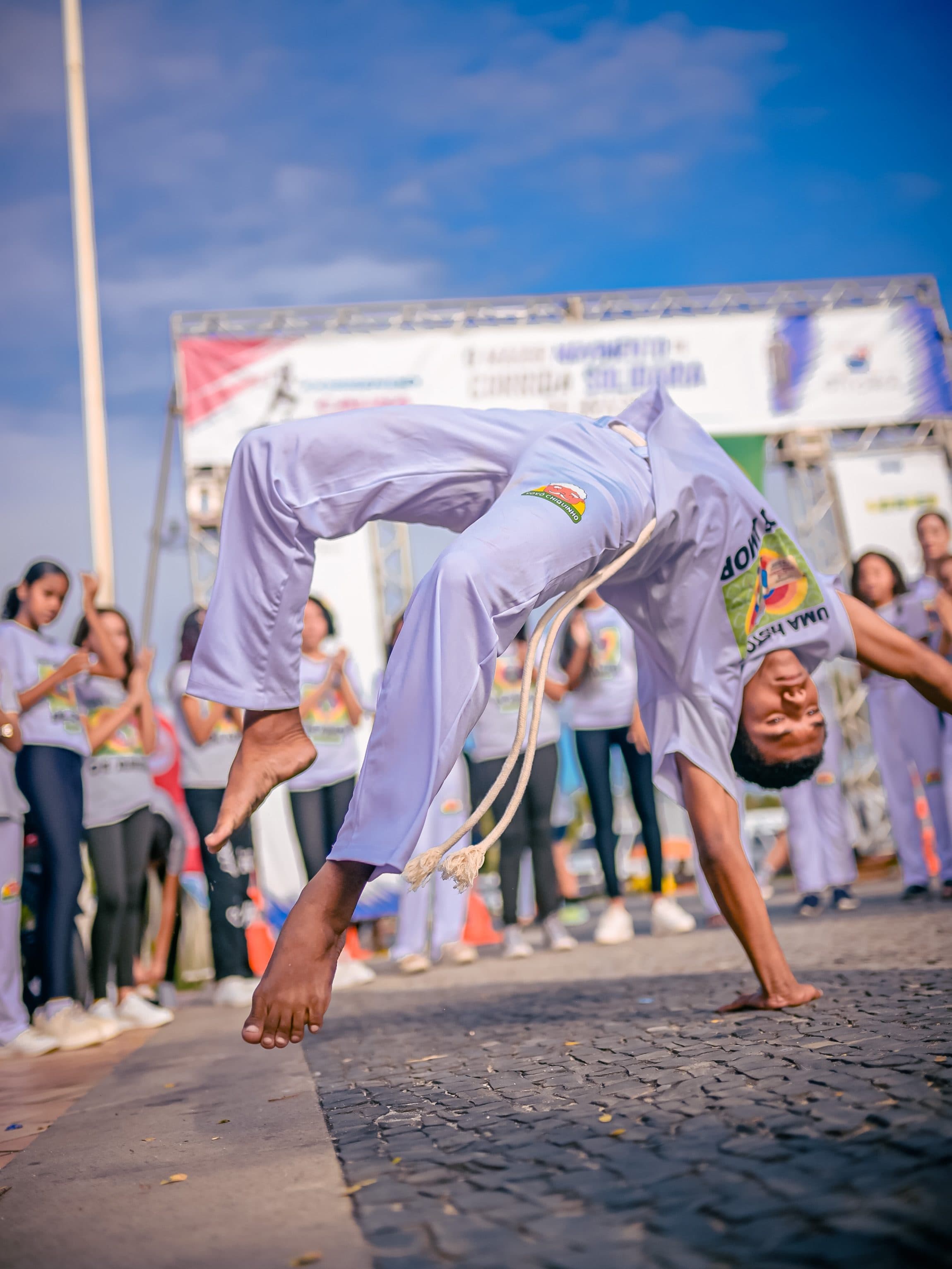 Jovem do instituto fazendo um movimento de capoeira no ar, diante da roda