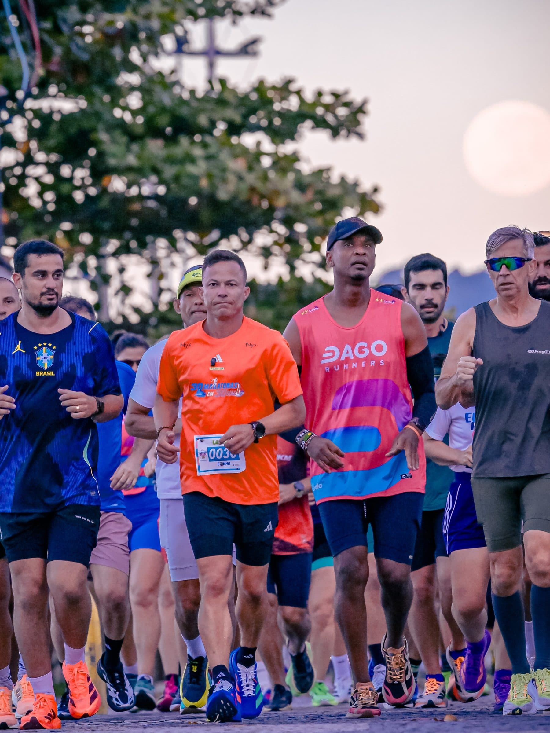 Edinho de camisa laranja liderando um pelotão de corredores na orla ao amanhecer