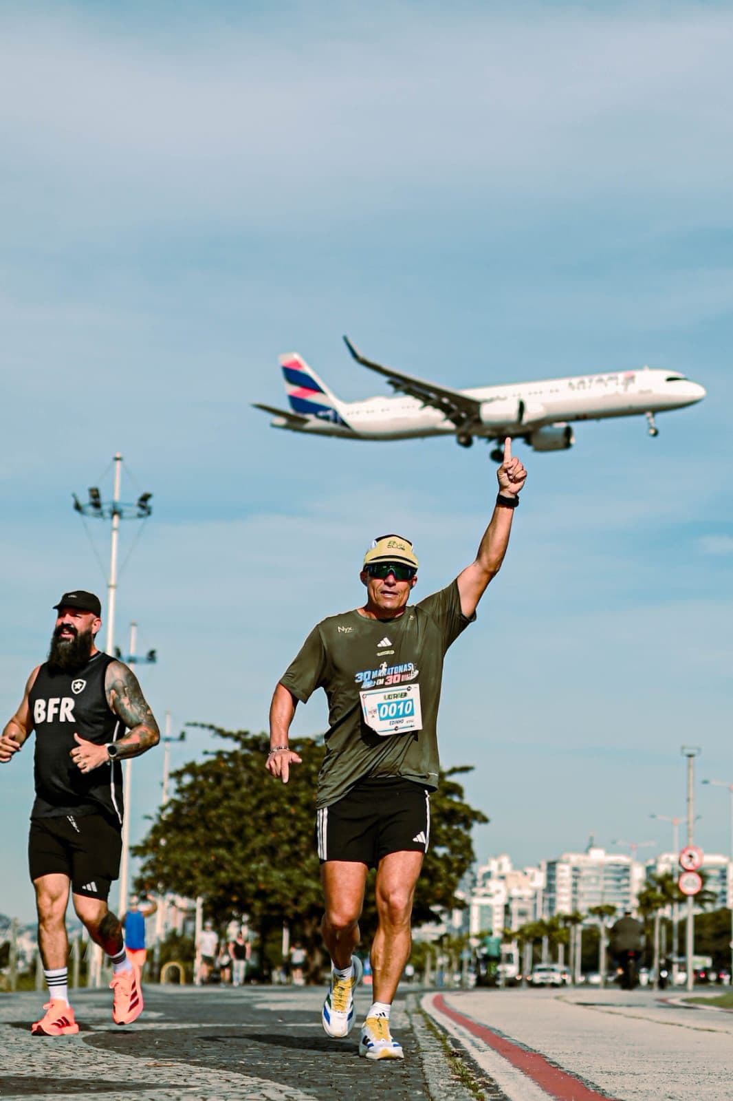 Edinho correndo na orla e apontando para um avião que passa baixo, durante as 30 maratonas