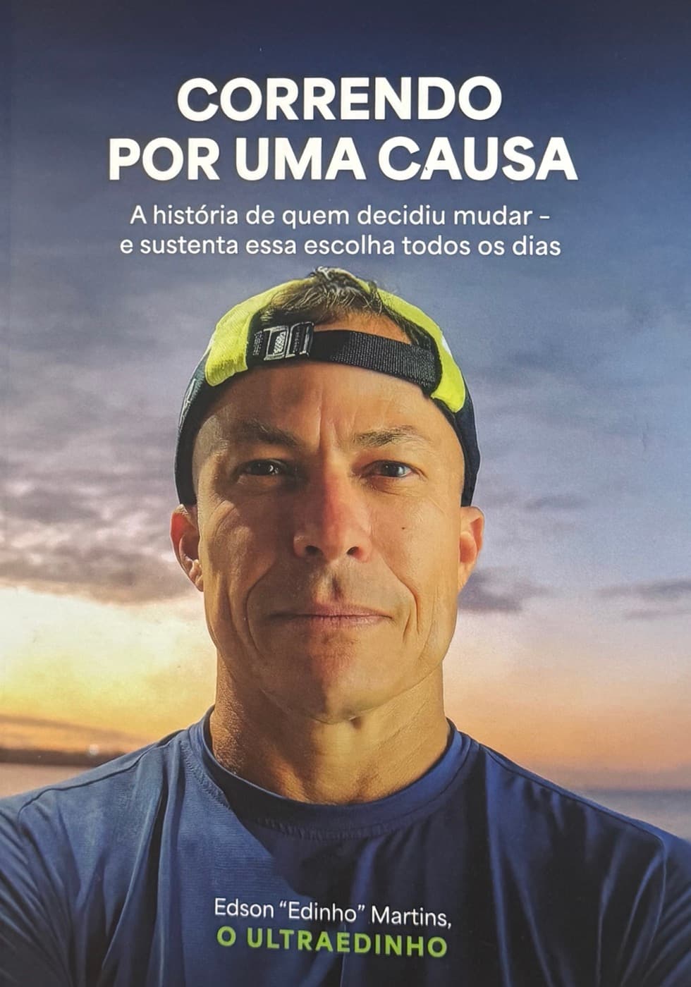 Capa do livro Correndo por uma Causa, de Edson Borges Martins: ele de boné virado pra trás, ao pôr do sol, com o título em destaque