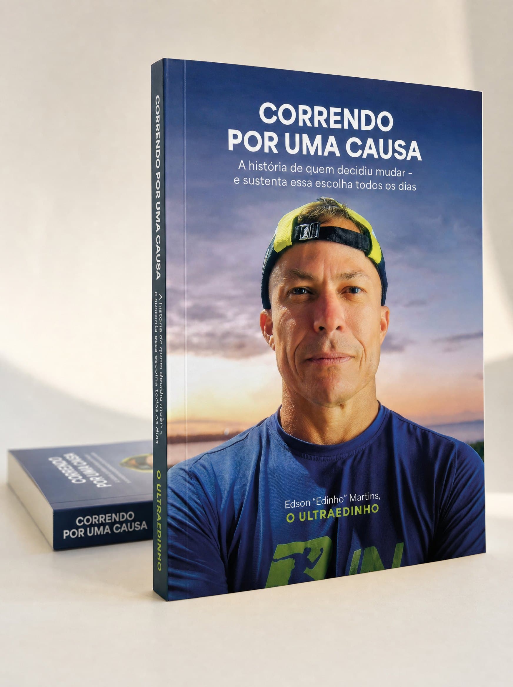 Livro físico Correndo por uma Causa, de Edson Borges Martins, em pé sobre superfície clara com um segundo exemplar deitado atrás, mostrando a capa e a lombada